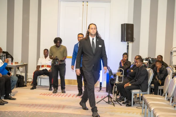 A brother in a black suit walks the aisle of the ceremony as members look on from either side.