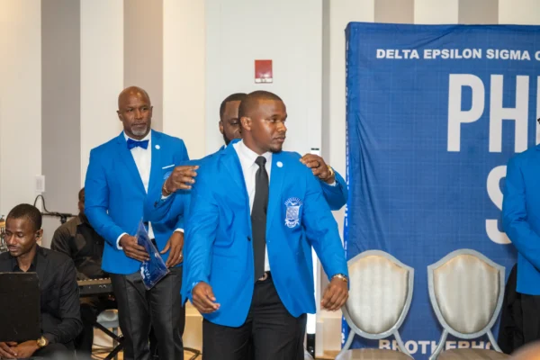Brothers in royal blue regalia take their place on stage as another brother is invested before the Phi Beta Sigma shields.